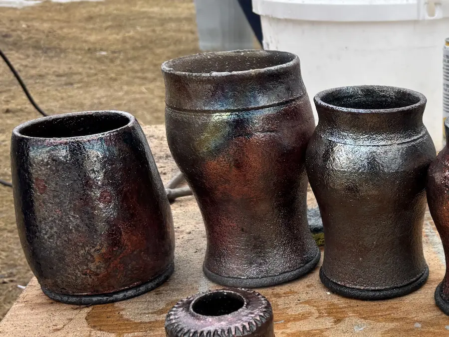 Three raku fired pots that are almost black with an iridescent metallic glaze look